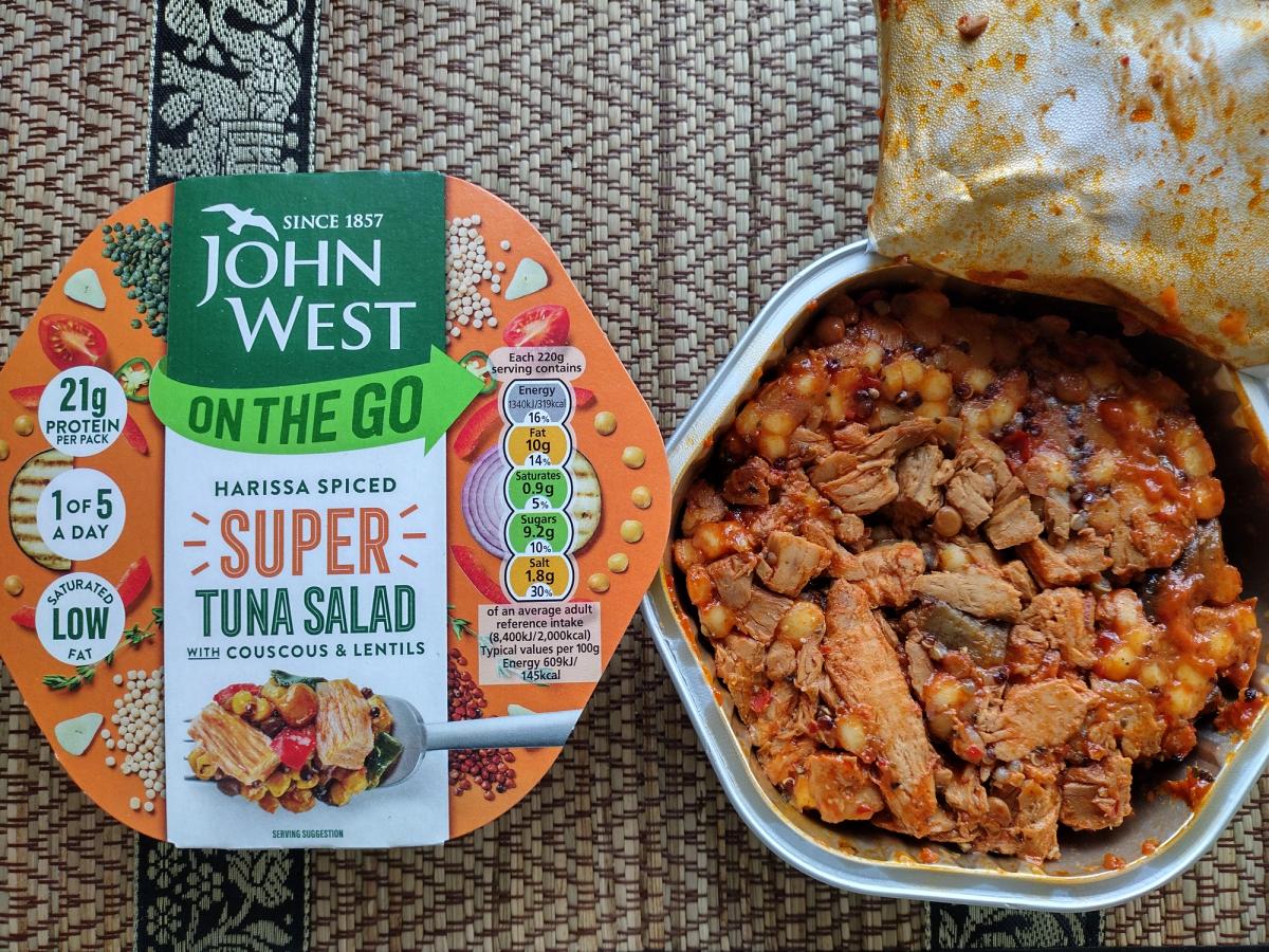 Open container of John West On The Go Super Tuna Salad Harissa Spiced next to packaging, showing large tuna chunks, giant couscous, and lentils.