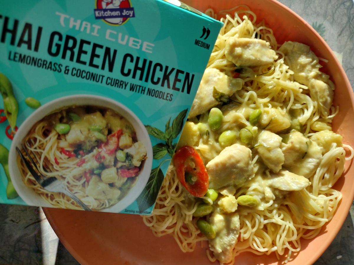 Review image of the Kitchen Joy Thai Cube Green Chicken with noodles. The finished dish shows the chicken, noodles, and green beans in a coconut curry sauce, placed next to the packaging for comparison.