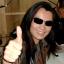 Tomonobu Itagaki, founder of Team Ninja, smiling in his signature sunglasses and giving a thumbs-up.