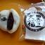 Cross section of a Yamamotoya Kuromame Daifuku on a yellow plate showing the thick white mochi skin embedded with whole black soybeans and a chunky red bean paste centre, alongside the open Japanese packaging.