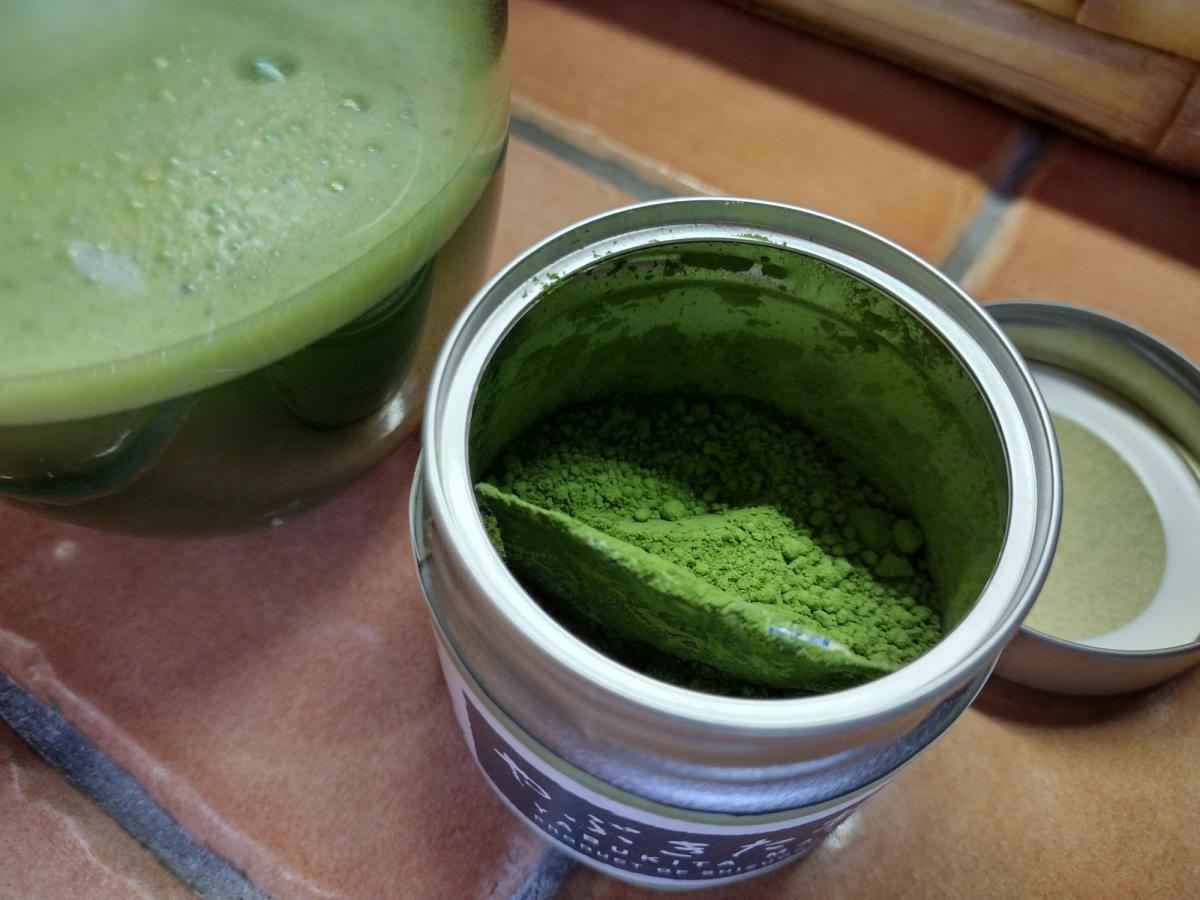Open tin of Ocha & Co. Single Cultivar Yabukita matcha showing vibrant green colour and fresh powder clumps next to prepared usucha.