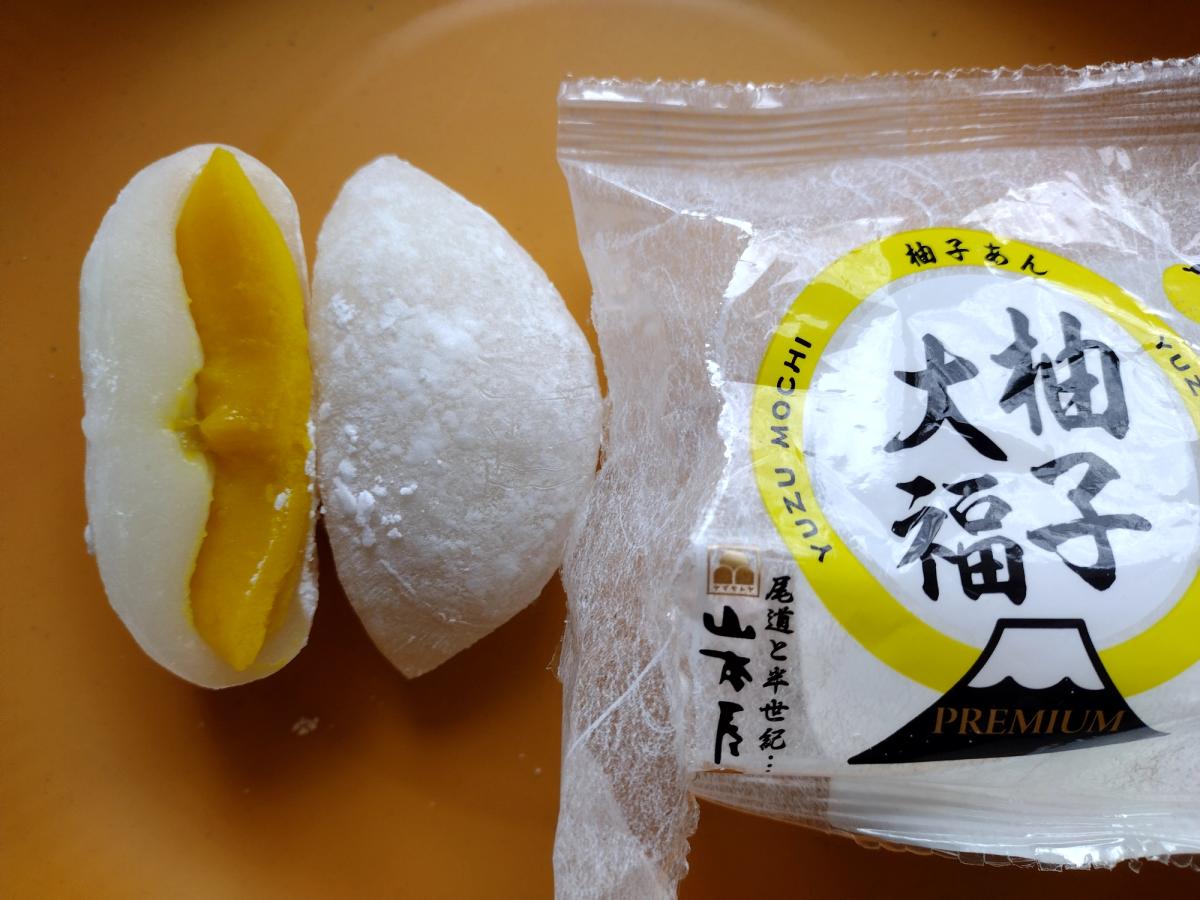 Cross section of a Yamamotoya Premium Yuzu Daifuku on a yellow plate, showing the bright yellow, smooth shiro-an and yuzu filling inside the white mochi dough, placed next to the open packaging.