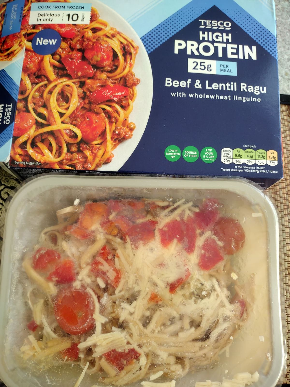 Tesco High Protein Beef & Lentil Ragu packaging alongside the frozen, uncooked meal in its plastic tray. The box highlights '25g Protein' and shows the cooked dish, while the tray reveals frozen linguine, ragu, peppers, tomatoes, and cheese under clear film.