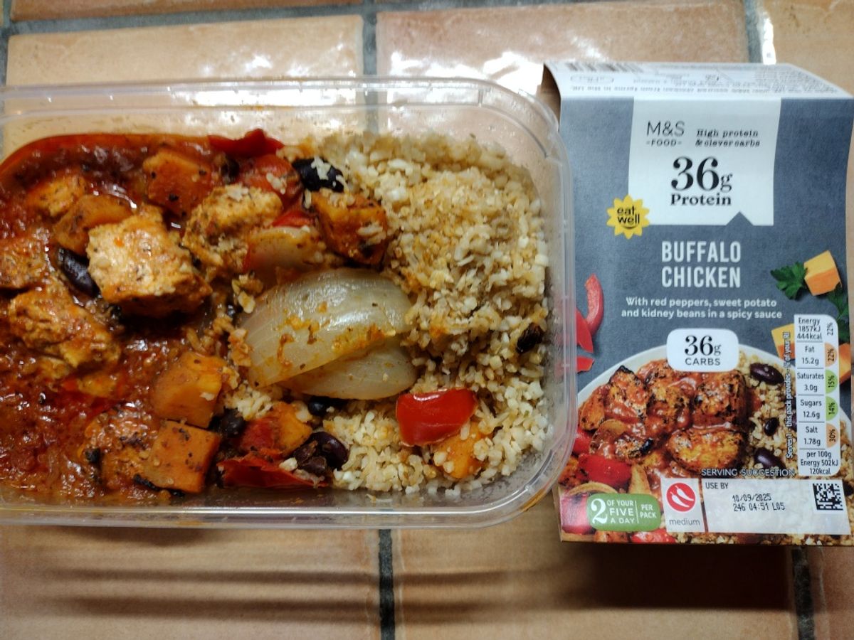 The prepared M&S Buffalo Chicken ready meal showing chunks of chicken in a spicy sauce with sweet potato, beans, and brown rice, alongside its M&S packaging.