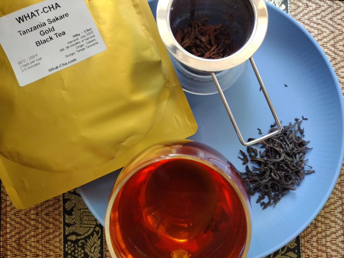 What-Cha Tanzania Sakare Gold Black Tea with clear copper-red brewed tea, loose twisted black tea leaves and spent leaves in a metal infuser.