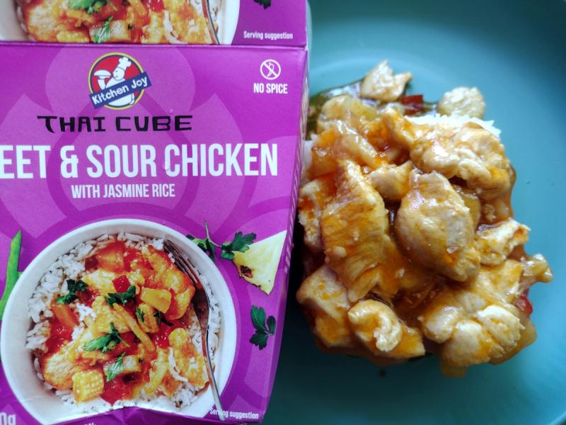 Review image of the Kitchen Joy Sweet & Sour Chicken from their Thai Cube range. The finished dish, featuring chicken in a glossy sauce over rice, is displayed next to the box to illustrate the ready meal's appearance.