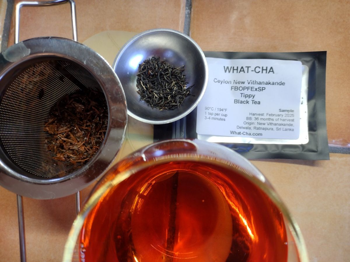 What-Cha Ceylon New Vithanakande FBOPFExSp Tippy Black Tea with dry and brewed leaves beside a deep amber-red cup.