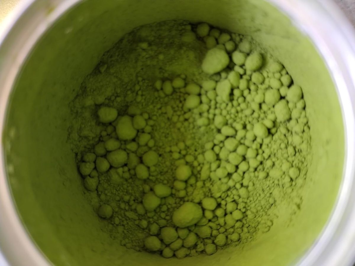 Close-up macro shot of bright green, fine matcha powder from a 'Limited Production Grown-For-Matcha Cultivar' in its tin