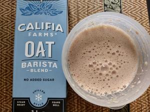 The Sneak Eats strawberry meal replacement shake mixed with Califia Farms Oat Barista Blend, showing a smooth and foamy texture in the shaker cup.