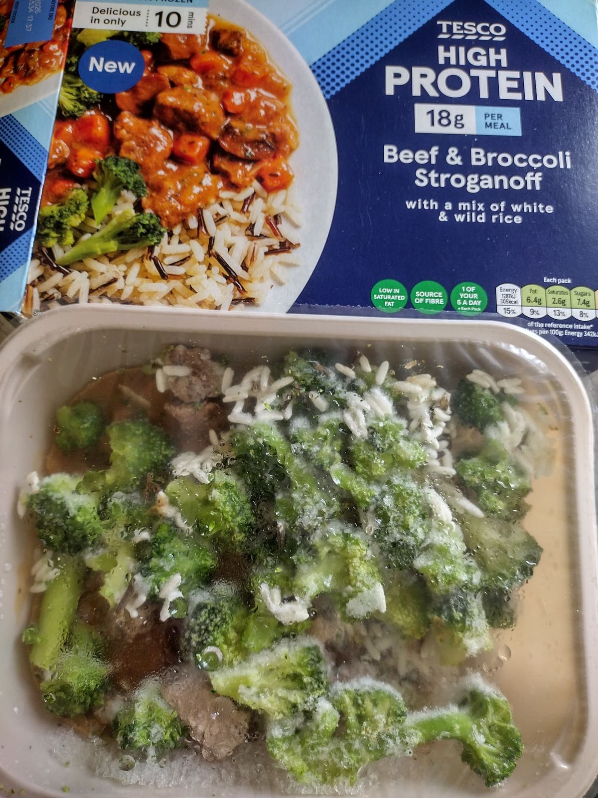 Cooked Tesco High Protein Beef & Broccoli Stroganoff served in its white plastic tray. The image features chunks of beef in a light brown stroganoff sauce, numerous bright green broccoli florets, and a mixture of white and wild rice.