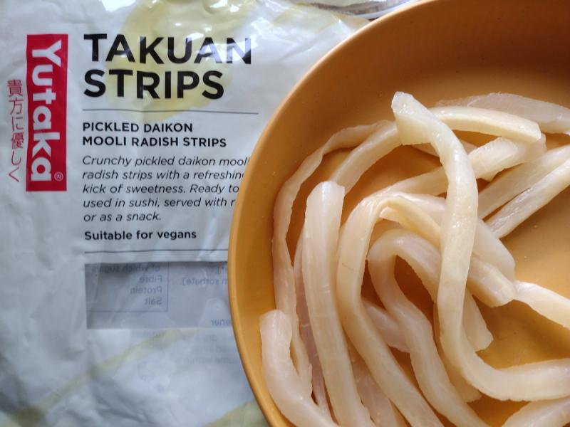 Close-up of Yutaka's pickled daikon mooli radish (takuan) strips served in a bowl, showing their crunchy texture.