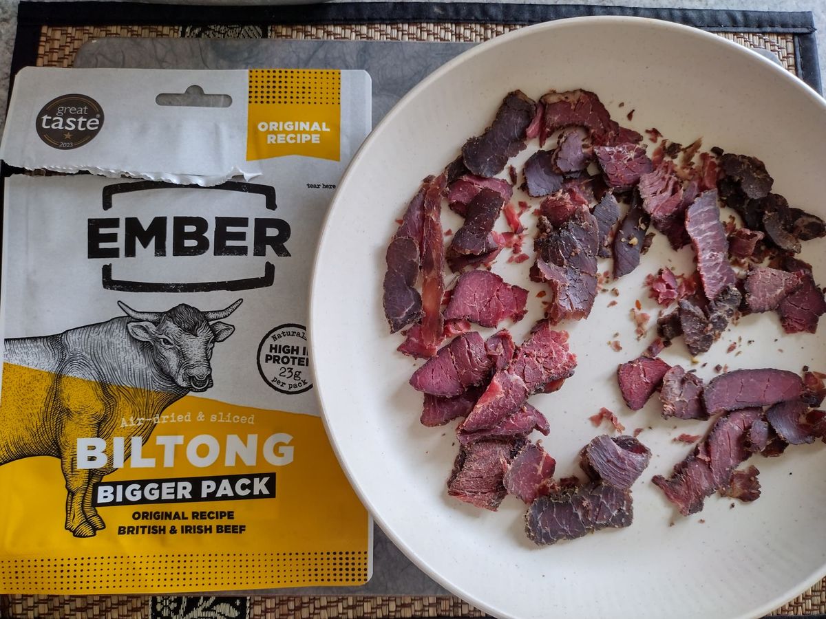 Packet of Ember Original Recipe Biltong (Bigger Pack) made from British & Irish beef, placed next to a white bowl filled with slices of the air-dried meat snack. The packaging shows a Great Taste 2020 award.