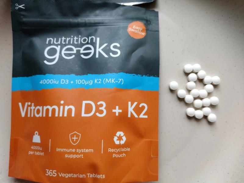 Nutrition Geeks Vitamin D3 4000IU + K2 MK-7 pouch next to a pile of small white micro tablets to show actual size.