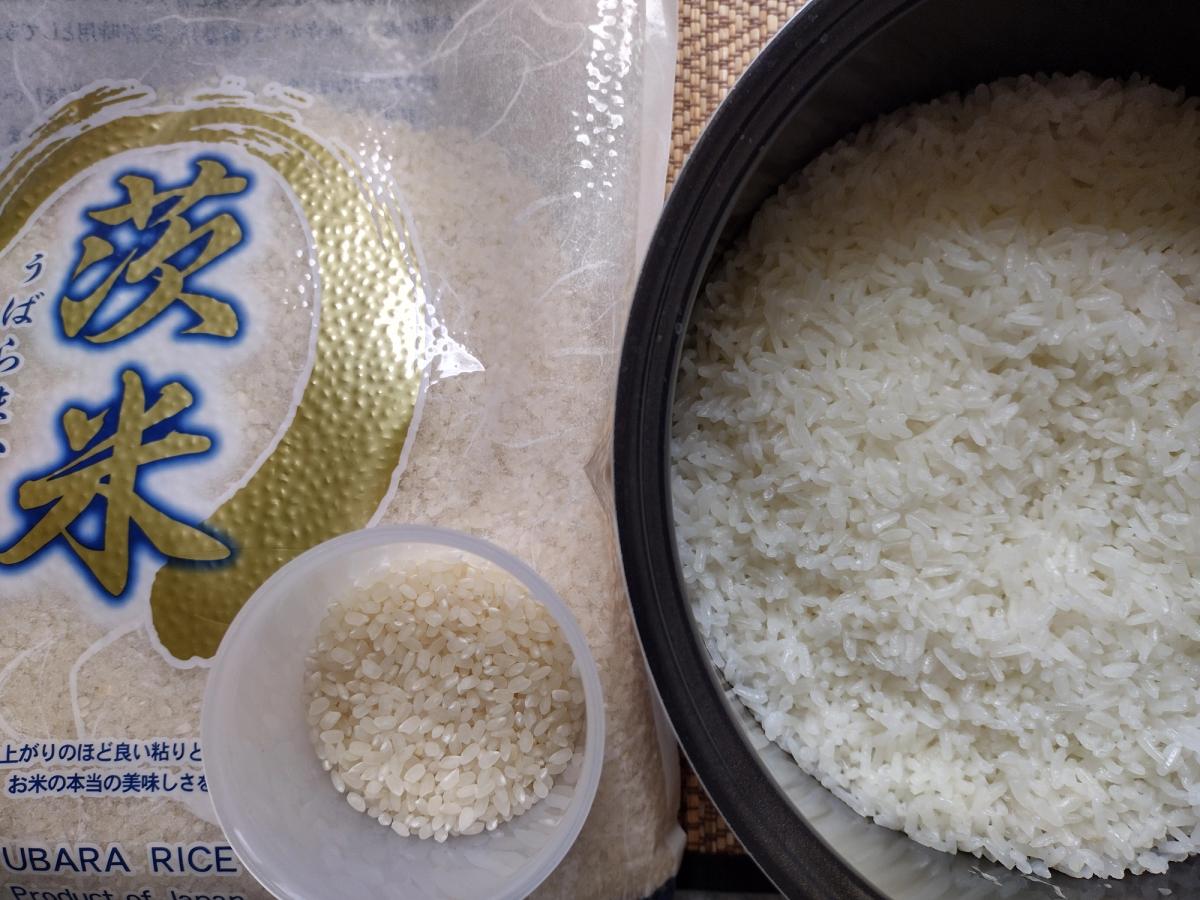 Bag of Ubara Rice from Ibaraki next to a rice cooker bowl showing fluffy cooked Niji no Kirameki grains compared to raw uncooked rice in a measuring cup.