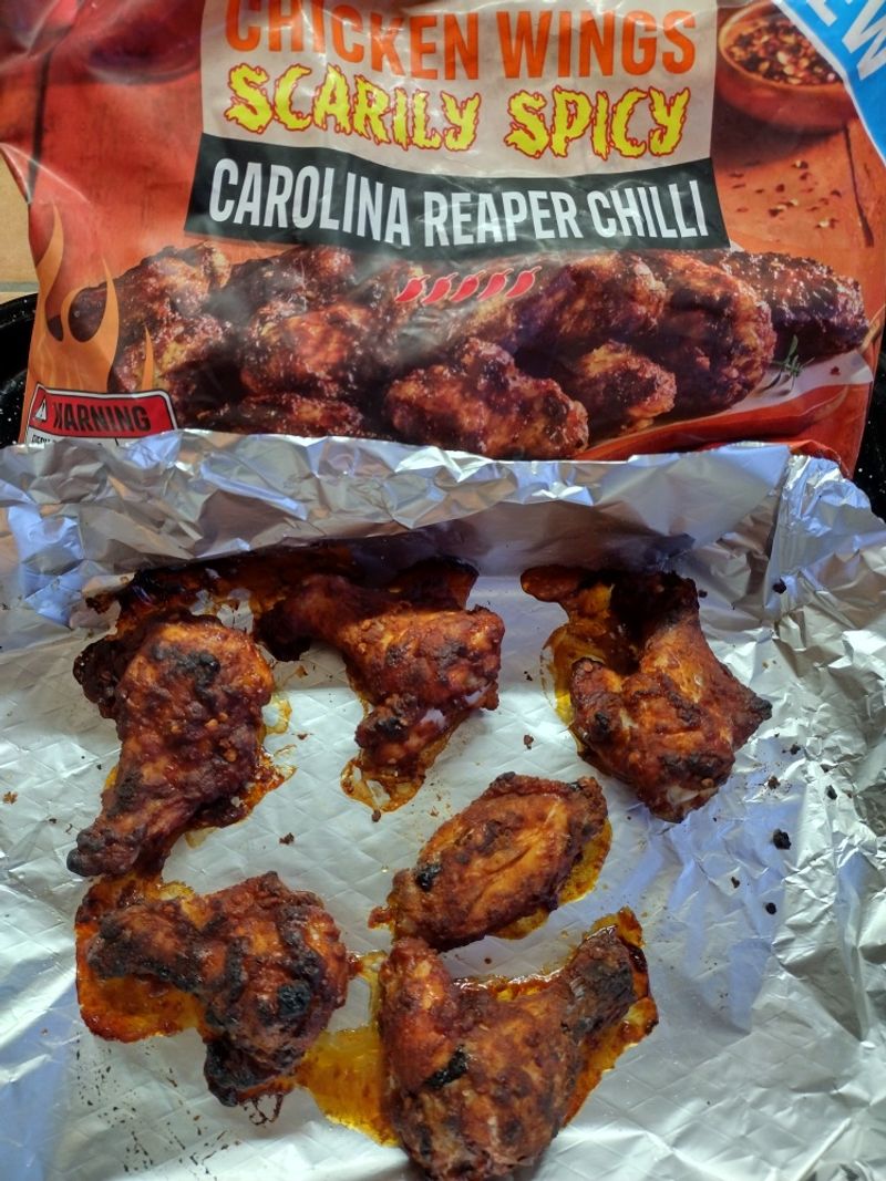 Cooked Iceland Scarily Spicy Carolina Reaper chicken wings on a foil-lined baking tray with the product packaging in the background.