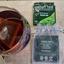 Tasting experience of organic Sabah Tea, showing the dark brewed liquor in a glass, the tea bag, and the vibrant green sachet from the single-estate Borneo plantation