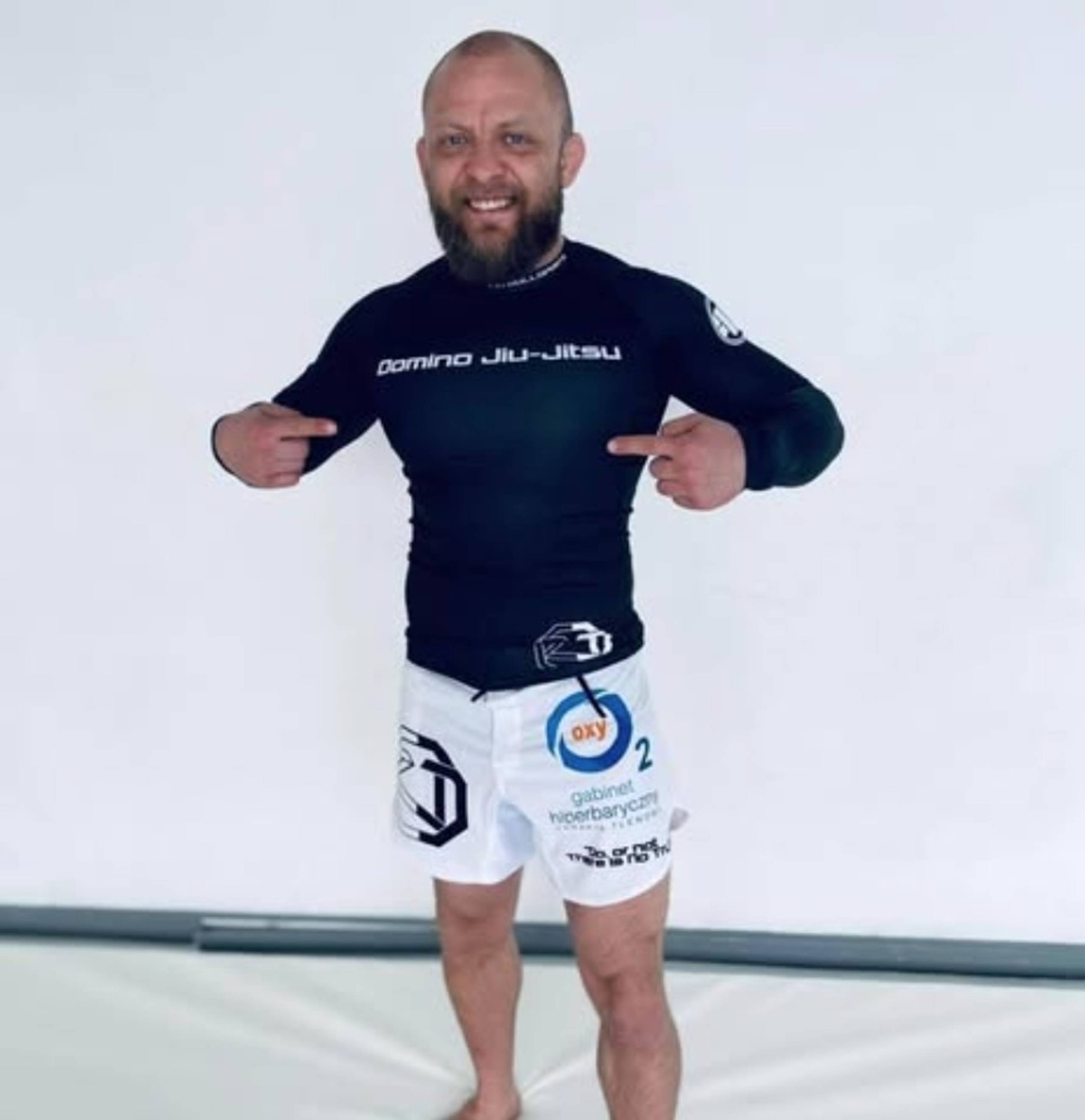 Mężczyzna w rashguardzie Domino Jiu-Jitsu wskazujący na klatkę