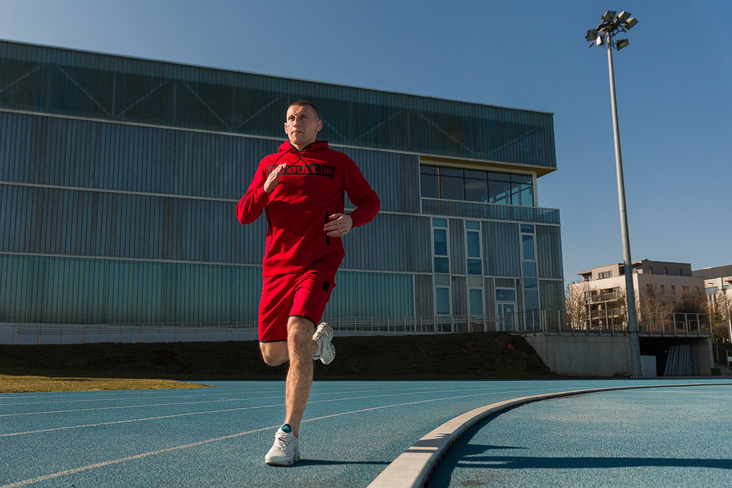 Man running in a red hoodie and shorts on a blue track