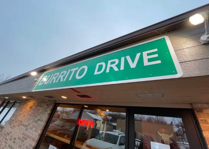 A green and white sign outside Burrito Drive restaurant displays its name.