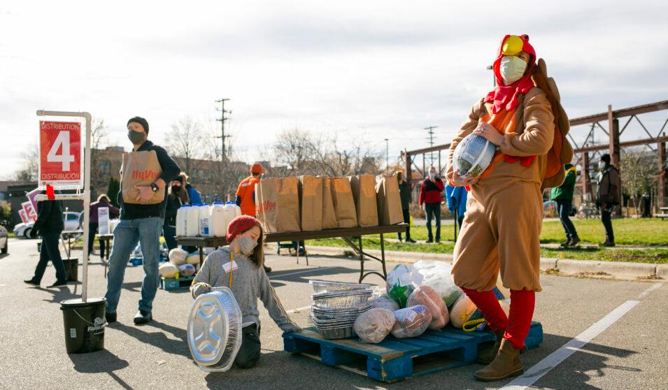 A group of people stand around a table with paper bags on it.