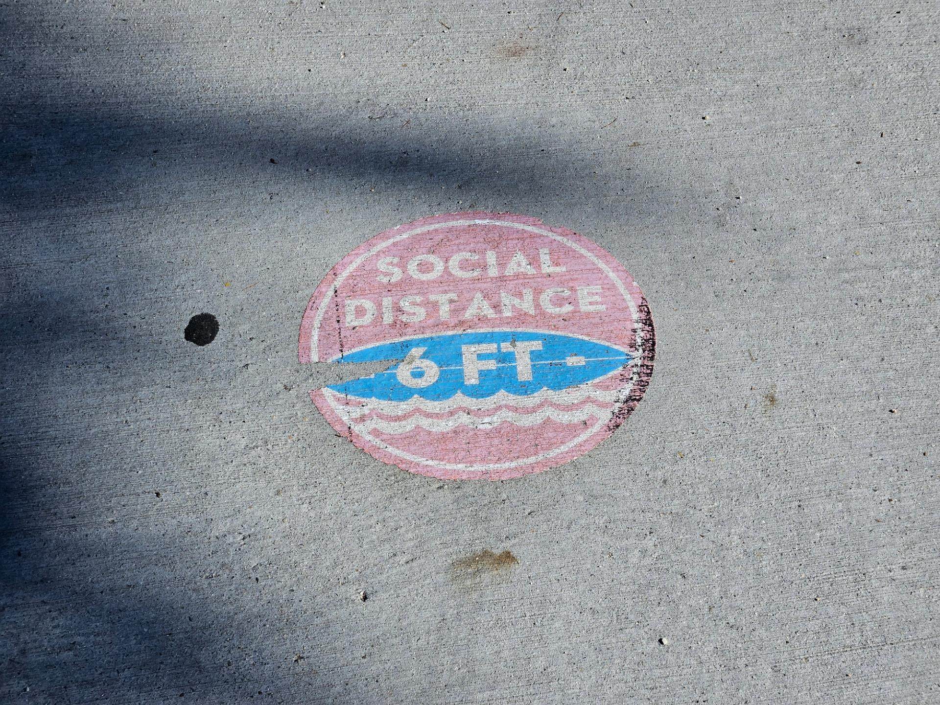 Marking on ground the says "Social Distancing - 6 Feet."