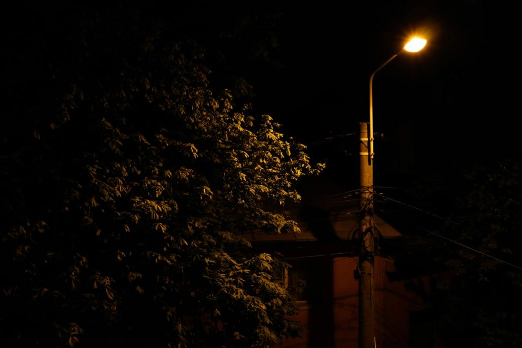 A lone streetlight barely illuminates the top of a tree at night. The photo is ominously lit with a yellow tint throughout.