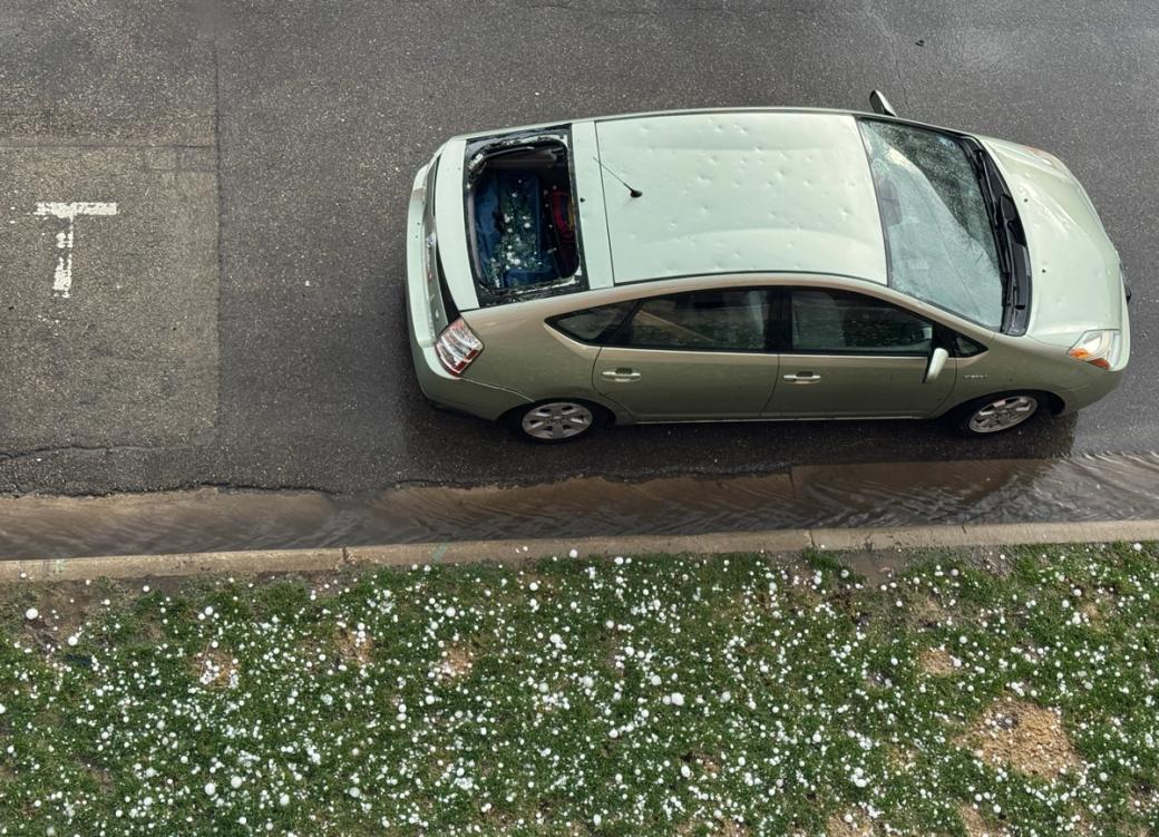 a green prius is parked on the street with visible hail damage and a broken back windshield