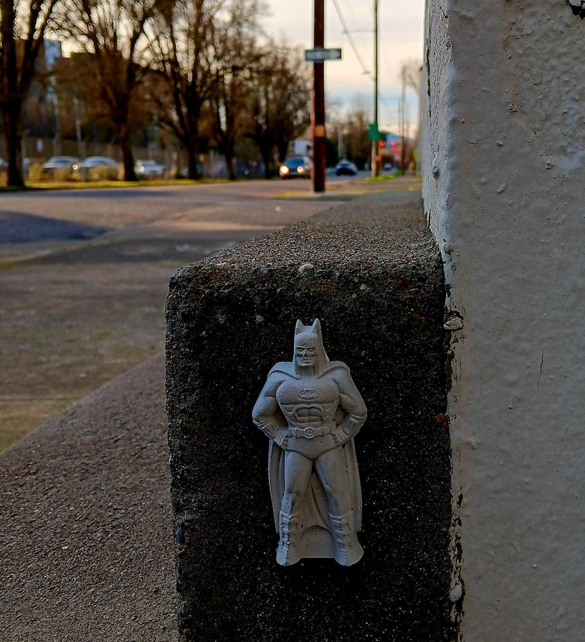 small white Batman figurine affixed to the corner of a building
