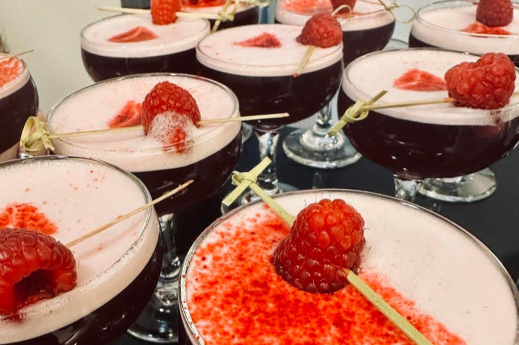 Multiple glasses of red cocktails topped with raspberries