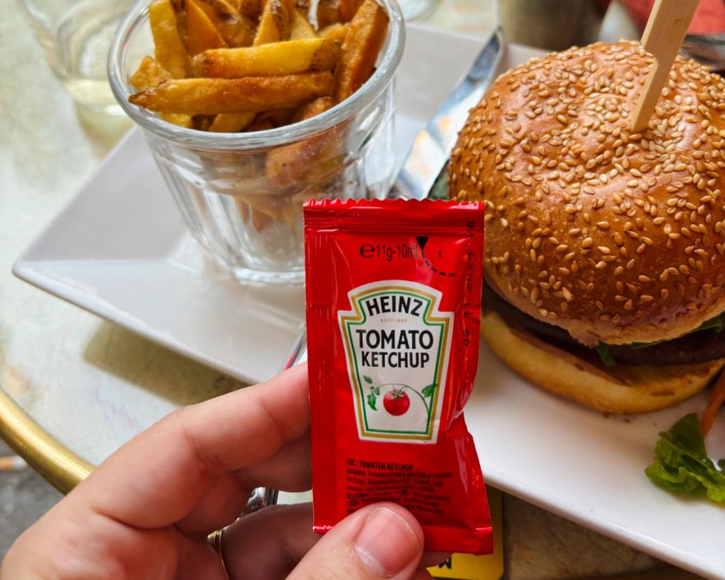 Heinz ketchup packet held in front of a veggie burger and French fries
