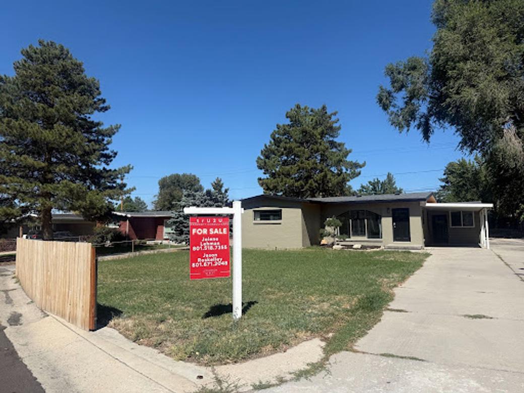 A red "for sale" sign is staked into a yard in front of a green house in Millcreek. 