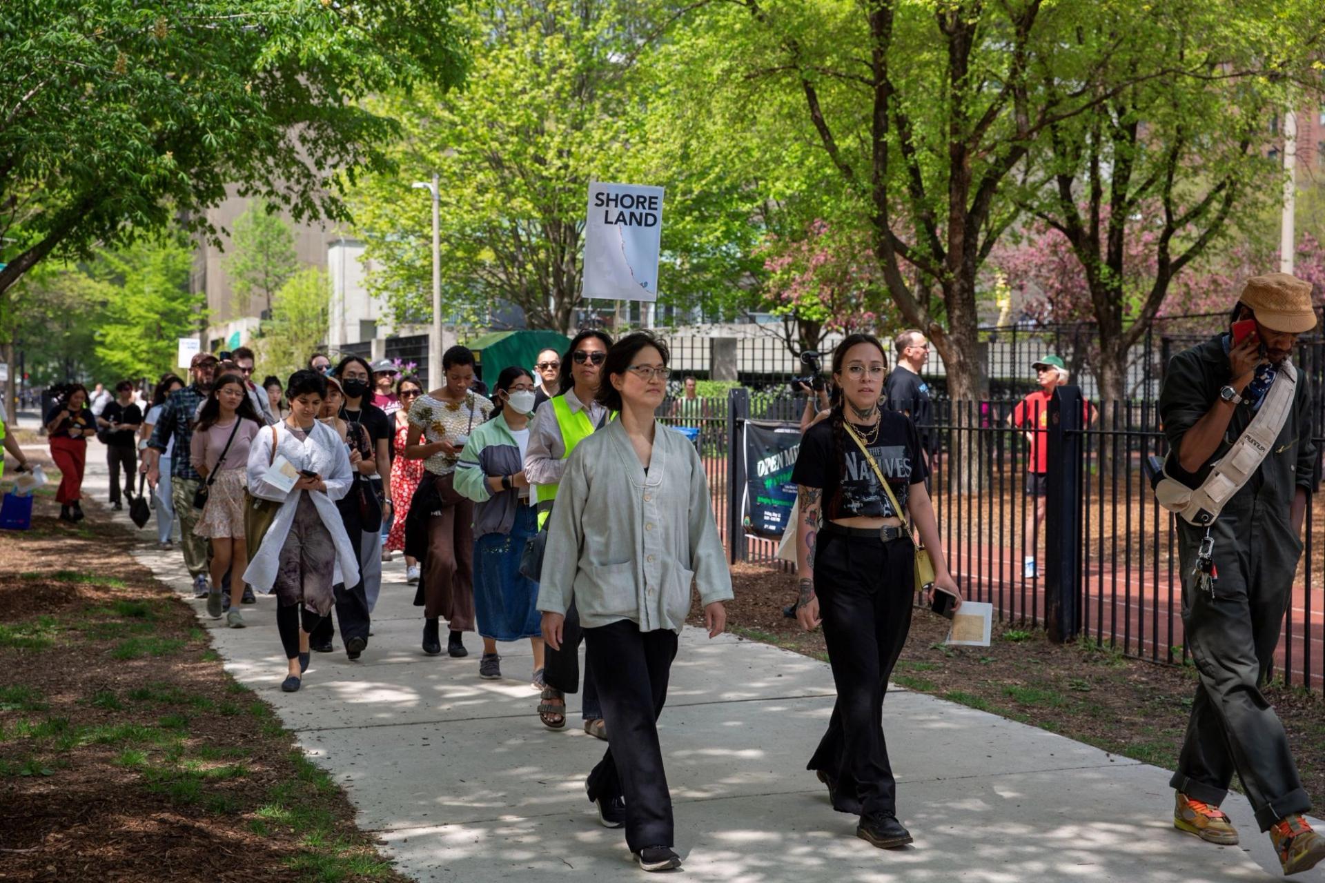 Two women lead a walking tour. One person holds a sign that says "Shoreland"
