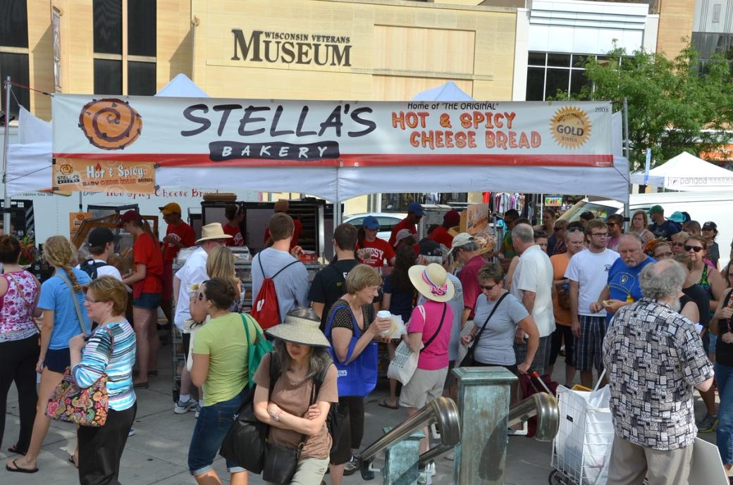 A crowd of people gather in front of a bakery storefront. 