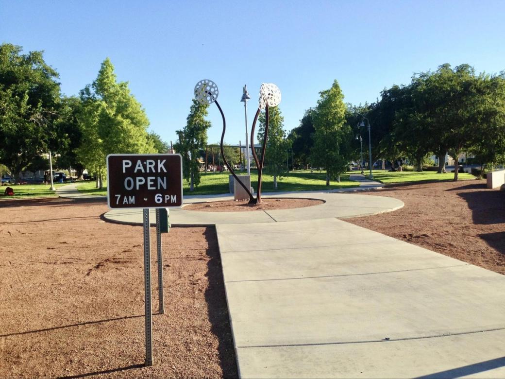 A brown sign at a park reads "Park Open 7 AM. - 6 PM"