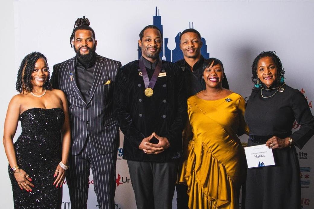 Six people standing posed for a photo. One of them is wearing is a gold medal in the middle