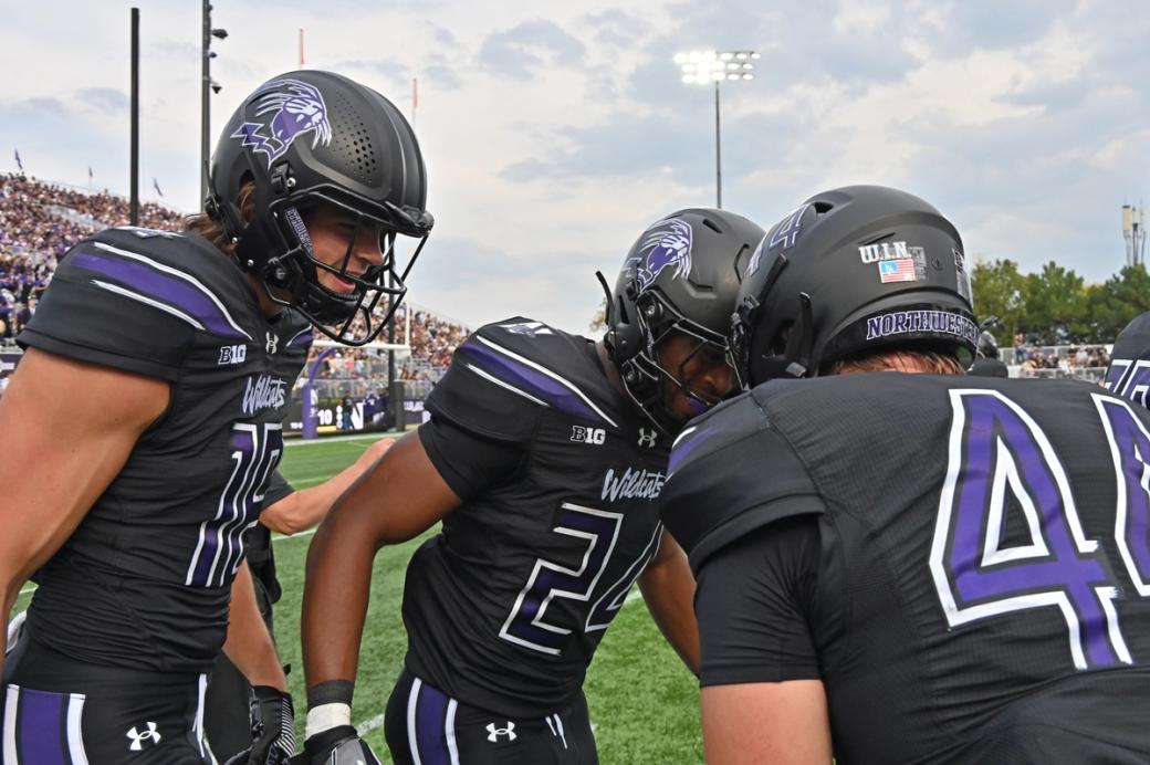 Three men in football attire and helmets talking with each other on a football field