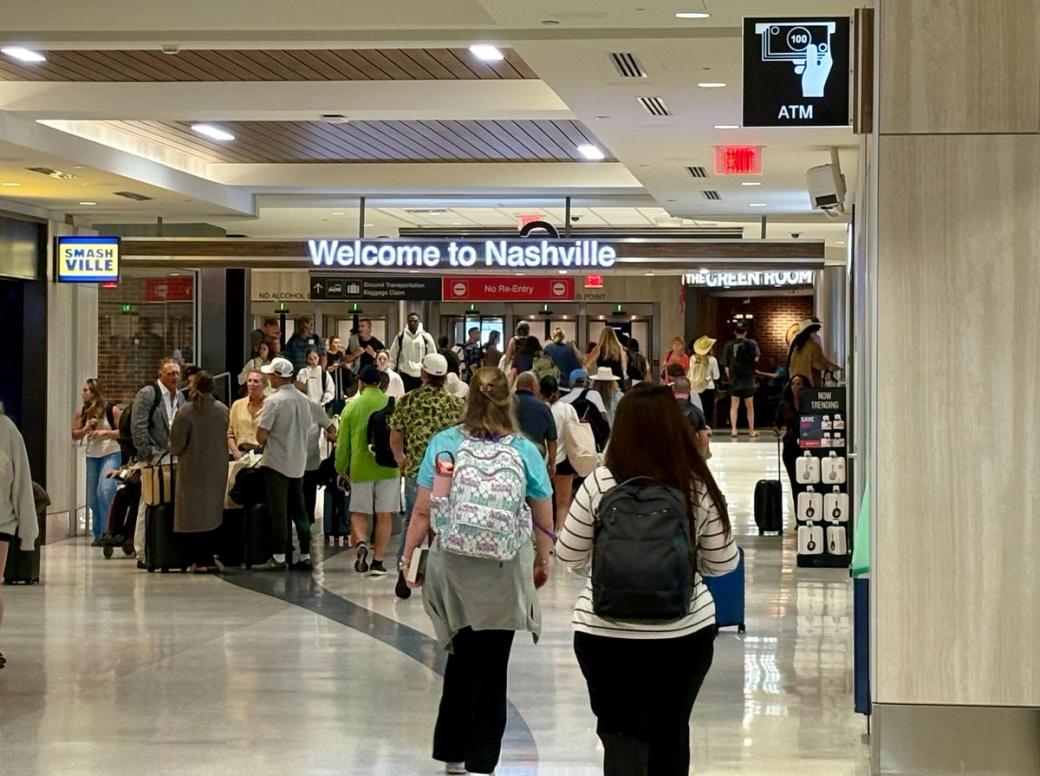People in an airport hallway, with a sign that says Welcome to Nashville.