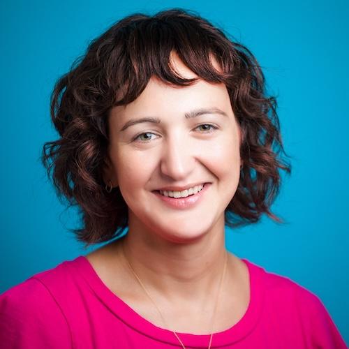 woman with short brown curly hair in pink shirt over blue backdrop