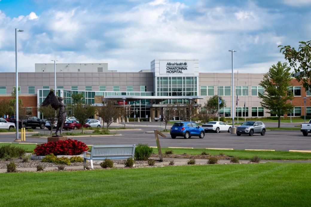A view of a large hospital building from the parking lot. There are cars parked and a statue on the left