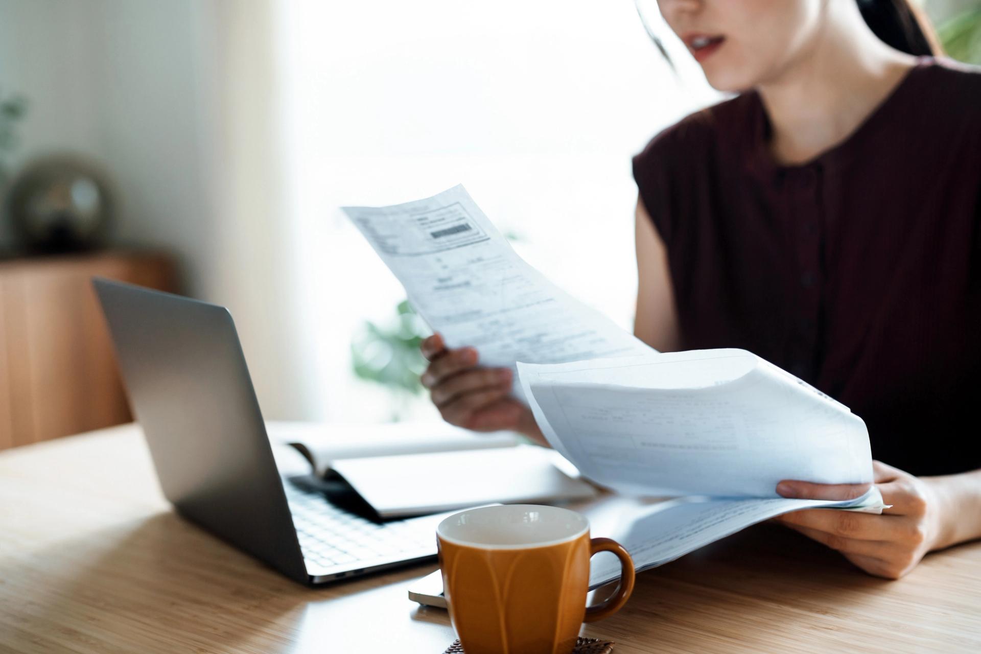 Cropped shot of Asian woman sitting at dining table, handling personal finance with laptop.