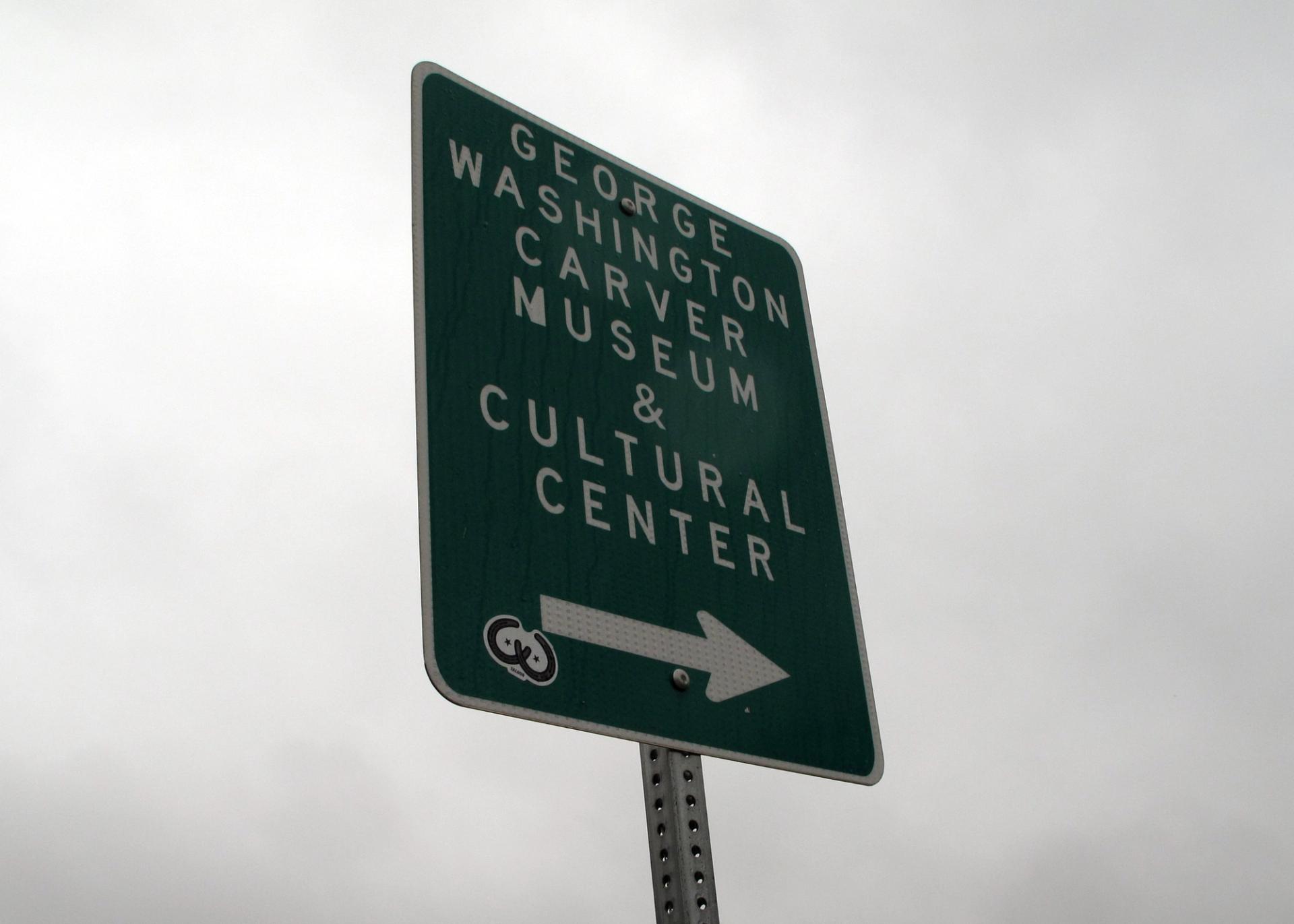A green sign that reads "George Washington Carver Museum & Cultural Center" with an arrow pointing to the right.