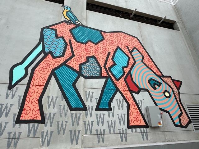 A mural on a building of a cow. The cow has patches of different shapes and colors - orange, turquoise.