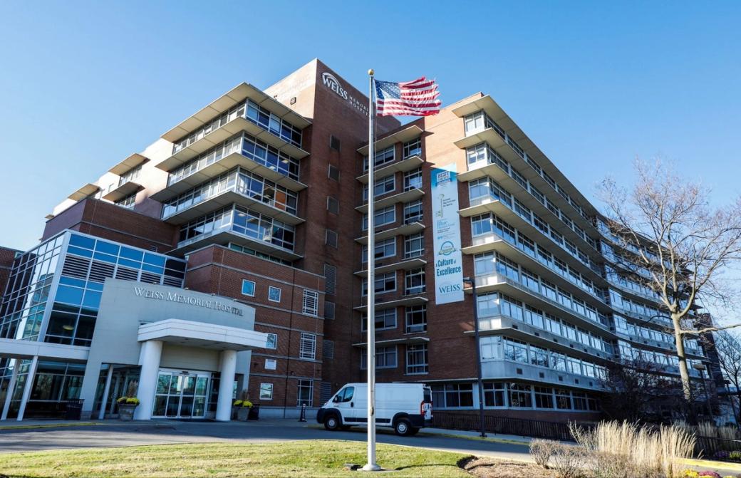 A multiple story building made of brick and with a lot of windows. There's a flag pole with an american flag in the foreground