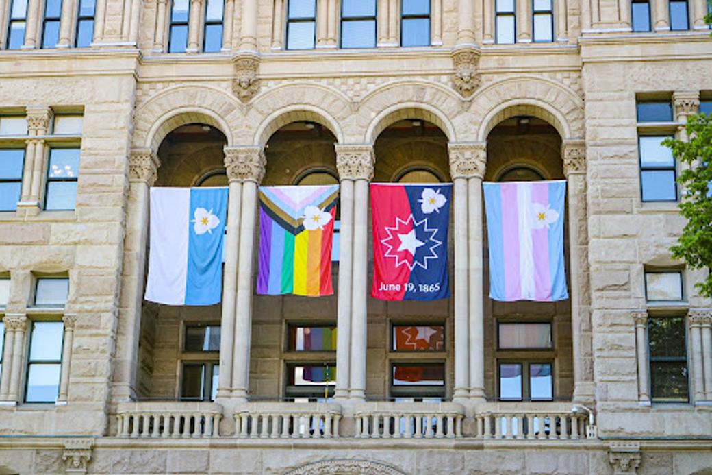 Four flags hang between the arches of the Salt Lake City and County Building: The Salt Lake City flag, Pride flag, Juneteenth flag, and transgender flag. 
