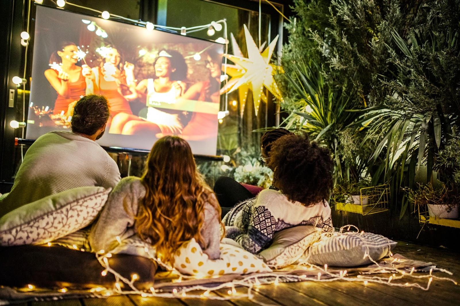 a group of three people is sitting around a screen for a movie