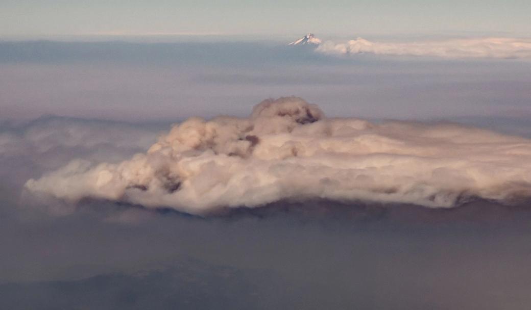This aerial view, taken from inside a commercial aircraft, shows the smoke pall of the active Grasshopper fire backdropped by Mount Hood in Oregon on August 5, 2026.