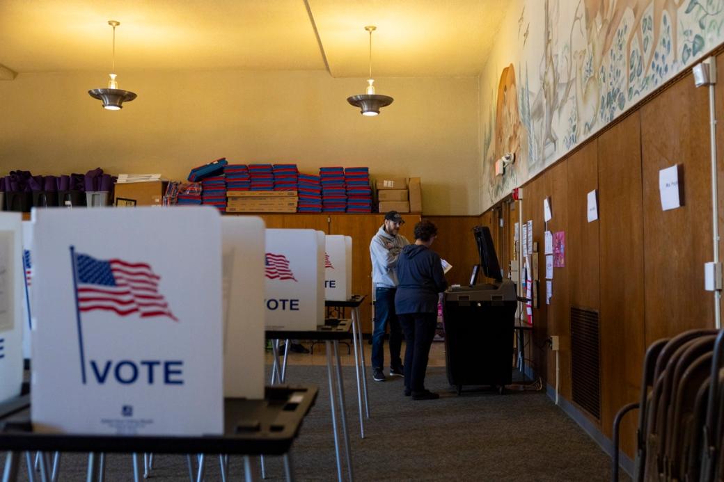 Lapham Elementary School during an election, poll workers in the back are working, voting booths cover the room.
