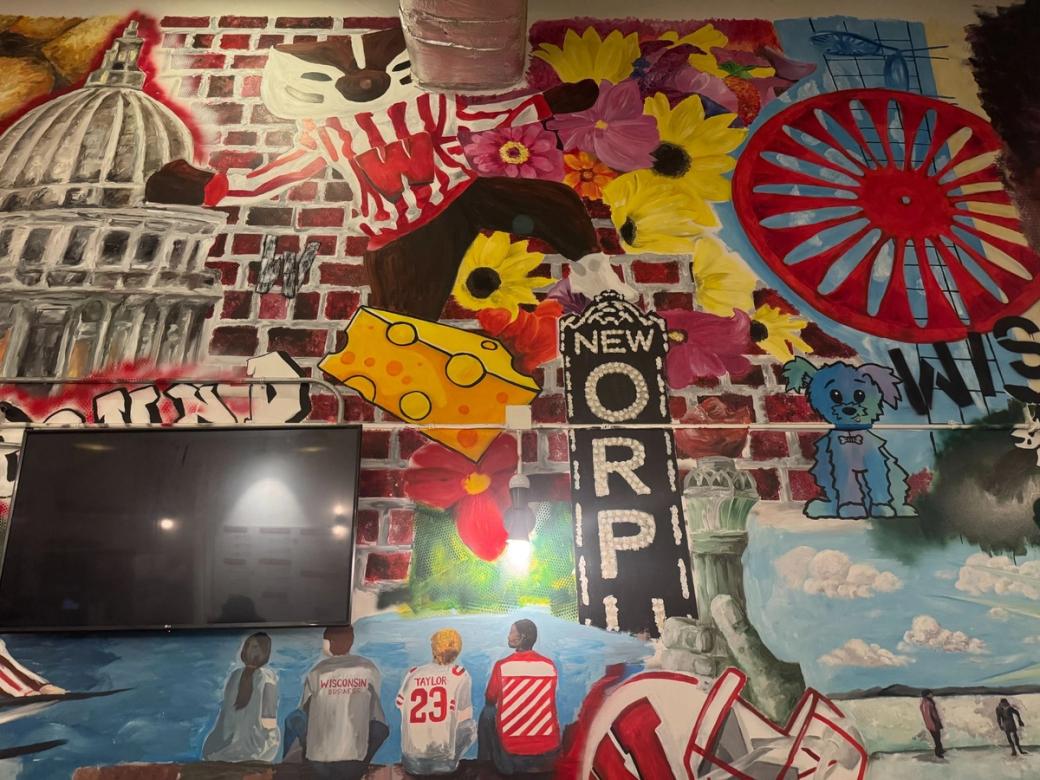 A colorful mural with an image of the state capitol, red bricks, a sign that reads "NEW ORPH..."