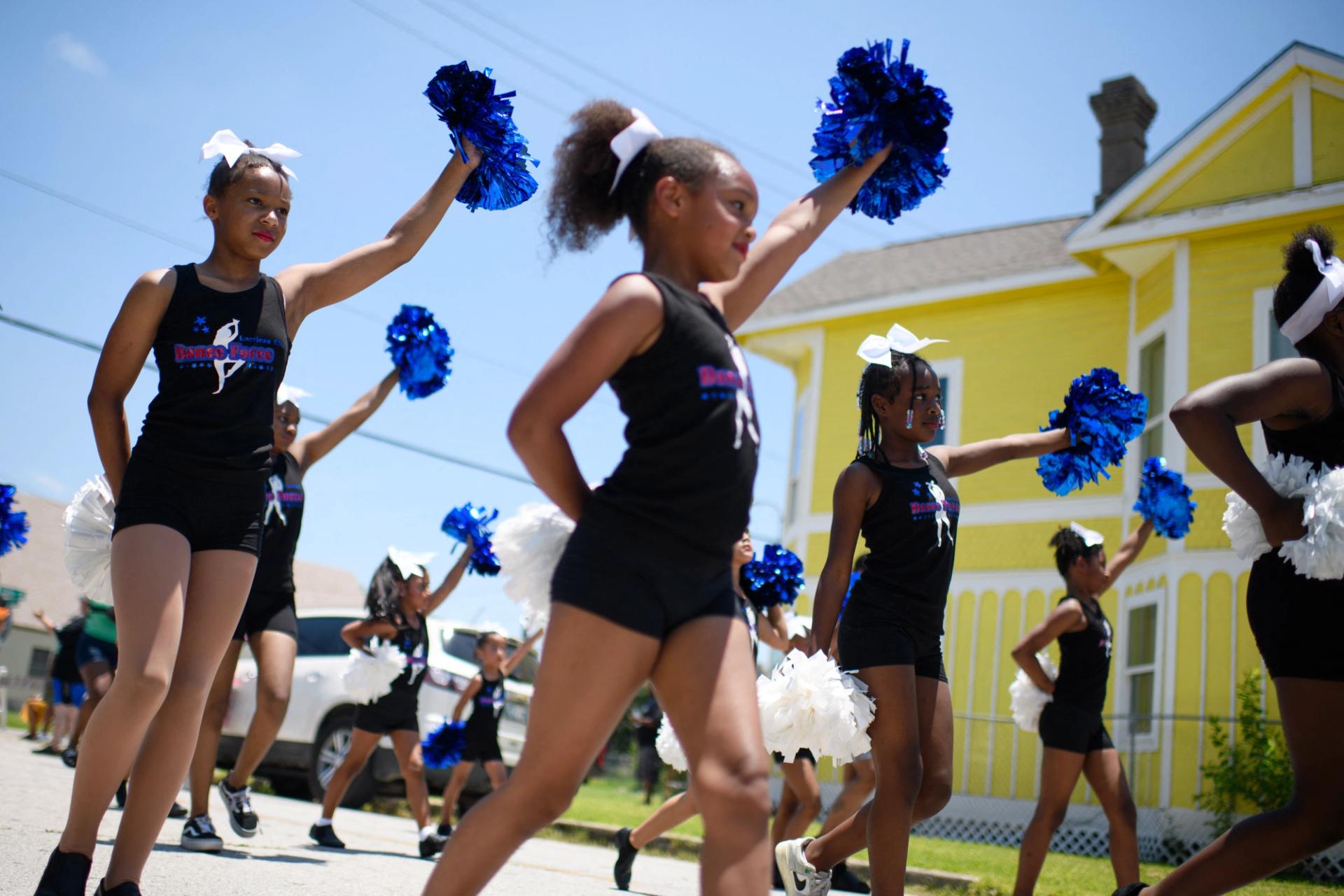 A group of girl cheerleaders holding up blue pom poms in a parade.