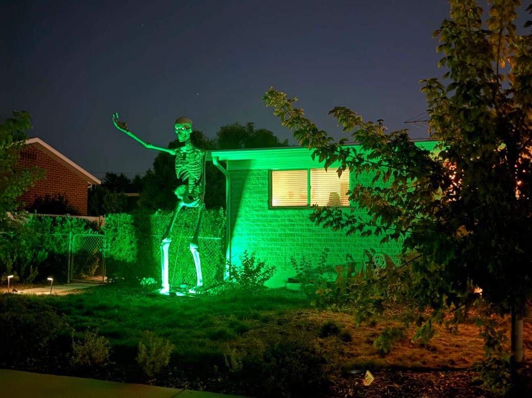 12-foot skeleton next to a house with a green light shining on it at night.
